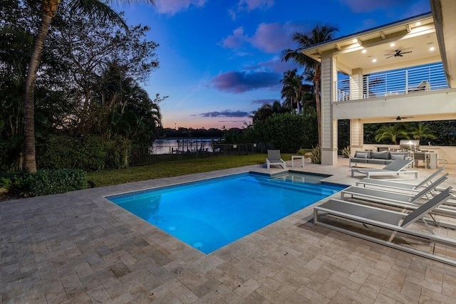 pool at dusk featuring area for grilling, ceiling fan, and a patio area