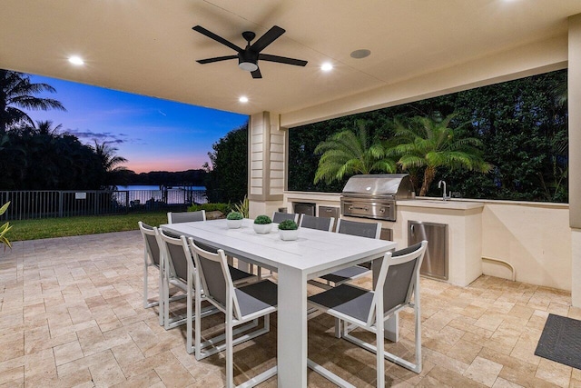 patio terrace at dusk with ceiling fan, area for grilling, exterior kitchen, and sink