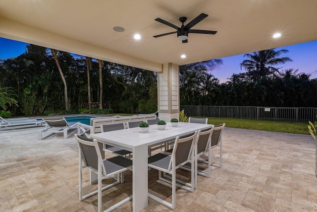 patio terrace at dusk featuring a fenced in pool and ceiling fan