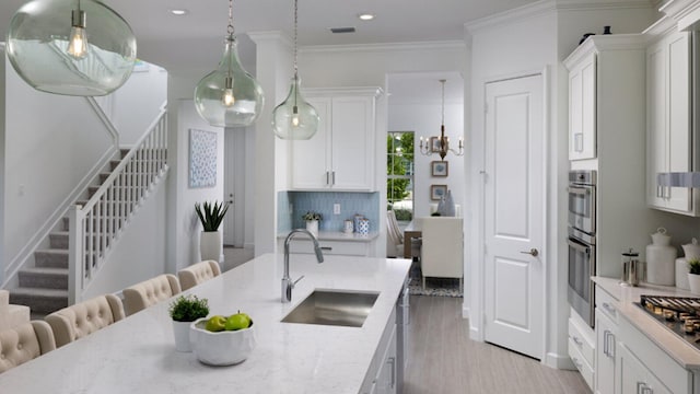 kitchen with decorative light fixtures, ornamental molding, white cabinets, a sink, and light stone countertops