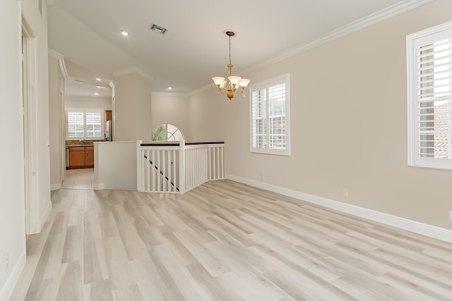 empty room featuring a chandelier, light hardwood / wood-style flooring, a wealth of natural light, and ornamental molding