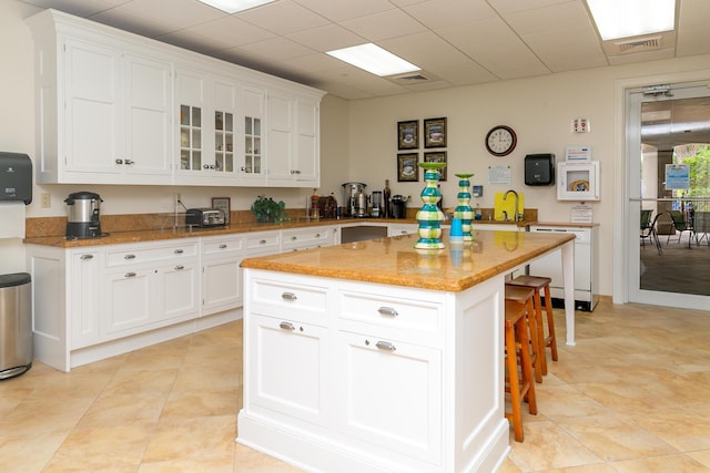 kitchen featuring a kitchen island, light stone counters, white dishwasher, a breakfast bar area, and white cabinets