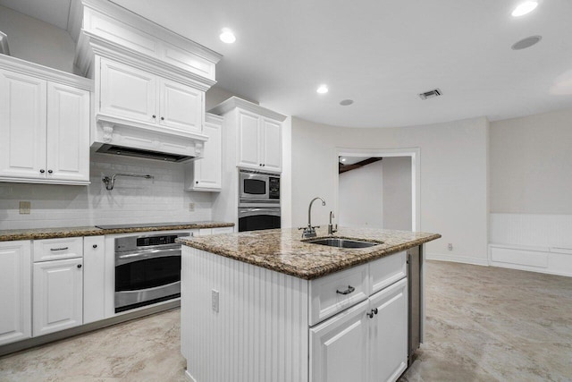 kitchen with stone counters, sink, white cabinetry, appliances with stainless steel finishes, and an island with sink