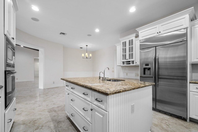 kitchen featuring a center island with sink, sink, built in appliances, white cabinets, and stone countertops