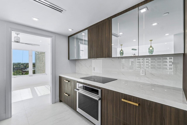 kitchen featuring stainless steel oven, black electric stovetop, decorative backsplash, decorative light fixtures, and light stone counters