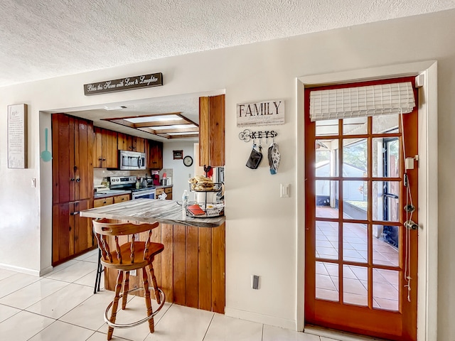 kitchen with light tile patterned floors, a textured ceiling, and appliances with stainless steel finishes