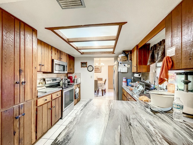 kitchen with decorative backsplash, appliances with stainless steel finishes, a skylight, light tile patterned floors, and a chandelier