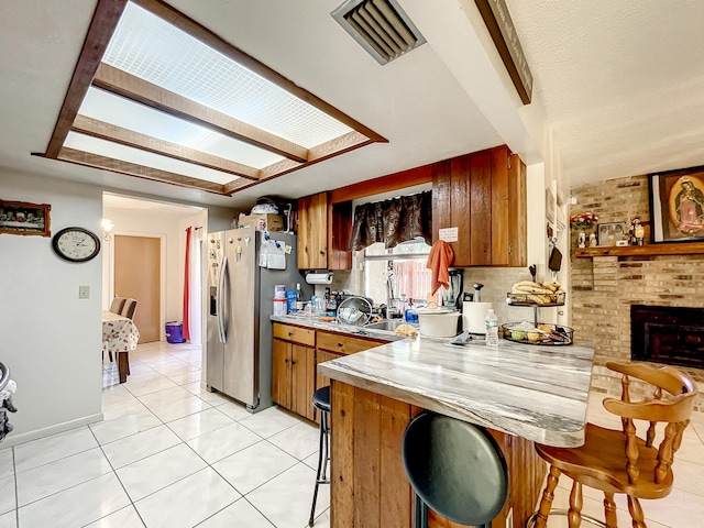 kitchen featuring kitchen peninsula, stainless steel fridge, a breakfast bar, a fireplace, and light tile patterned flooring