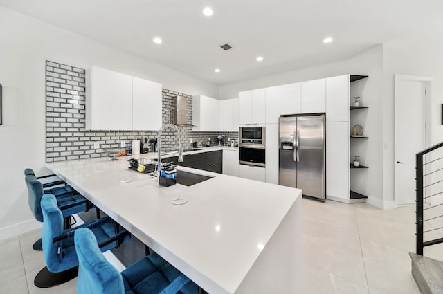 kitchen featuring kitchen peninsula, decorative backsplash, stainless steel appliances, and wall chimney range hood