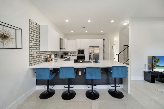 kitchen with kitchen peninsula, stainless steel fridge, a kitchen bar, decorative backsplash, and white cabinets