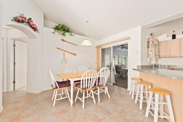 tiled dining area featuring a textured ceiling, ceiling fan, sink, and vaulted ceiling