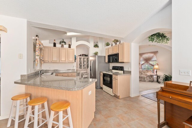 kitchen with a breakfast bar, white electric range, sink, a textured ceiling, and light brown cabinetry