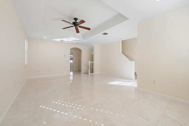 spare room featuring arched walkways, ceiling fan, baseboards, and a tray ceiling