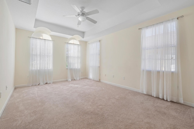 empty room featuring ceiling fan, light colored carpet, plenty of natural light, and a tray ceiling