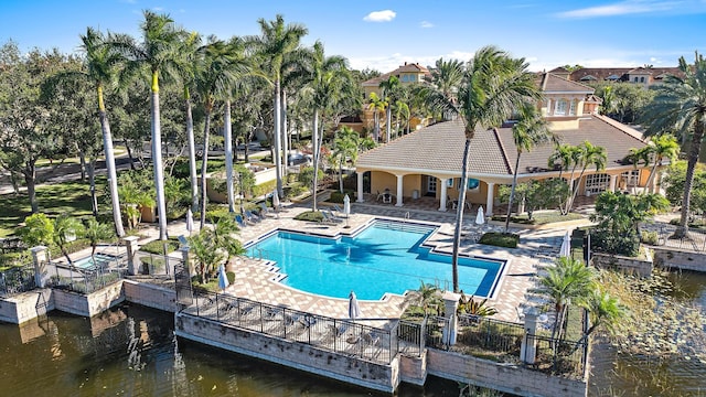 community pool with a patio area, fence, and a water view