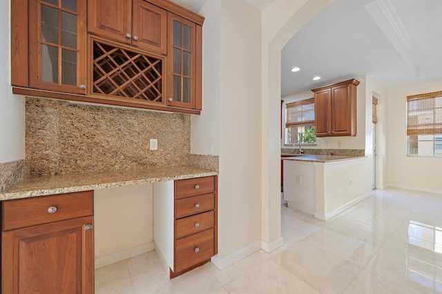 kitchen featuring light tile patterned floors, tasteful backsplash, built in desk, light stone counters, and sink