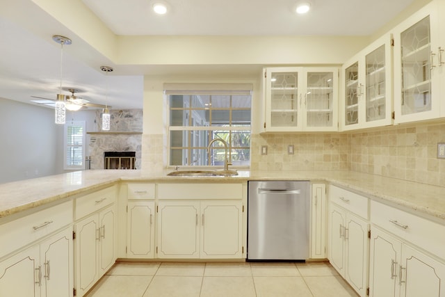 kitchen featuring light stone countertops, ceiling fan, sink, dishwasher, and a stone fireplace