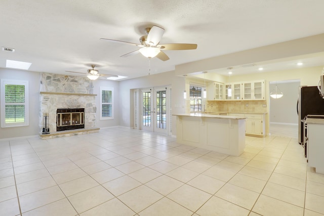 kitchen featuring french doors, white cabinets, ceiling fan, light tile patterned floors, and a fireplace