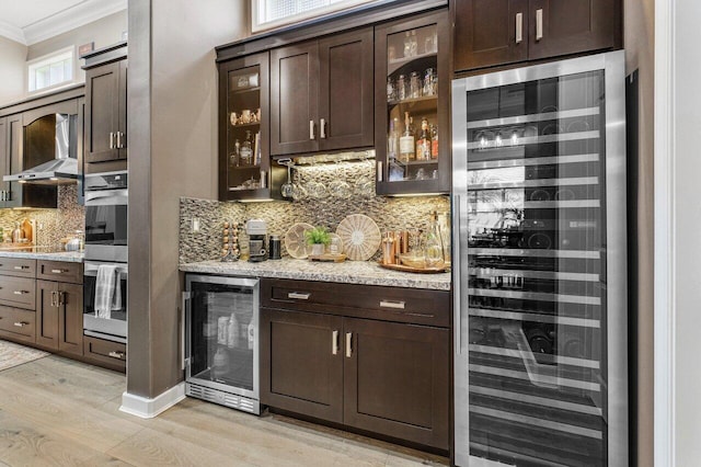 bar with light stone counters, dark brown cabinets, and beverage cooler