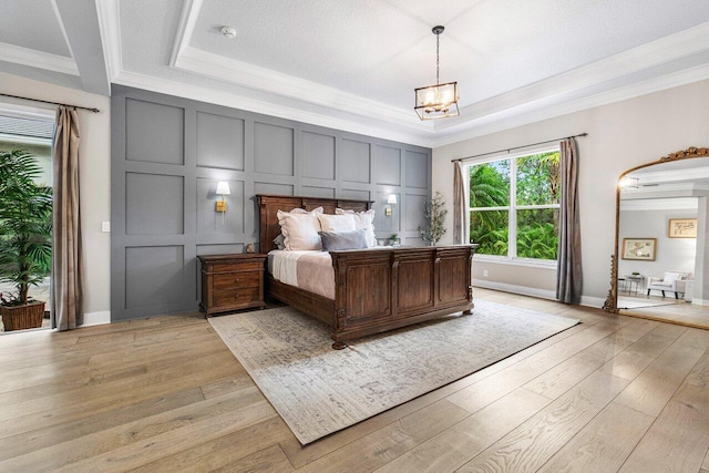 bedroom featuring a raised ceiling, an inviting chandelier, ornamental molding, and light wood-type flooring