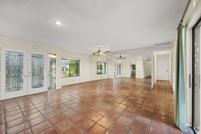 interior space with a textured ceiling, a chandelier, french doors, and dark tile patterned floors