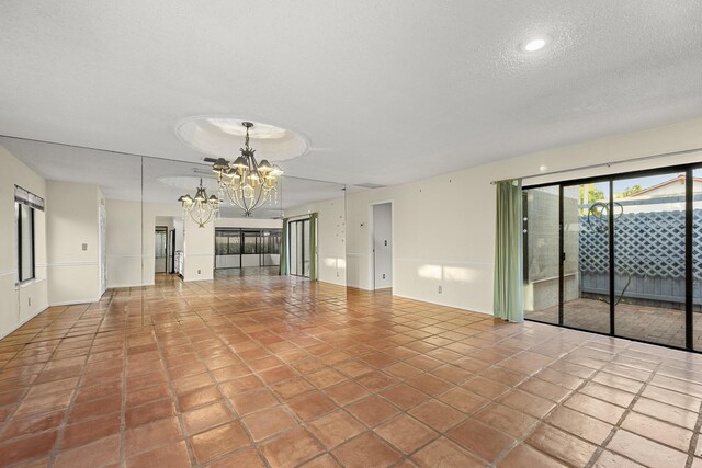 tiled empty room featuring a textured ceiling and a chandelier