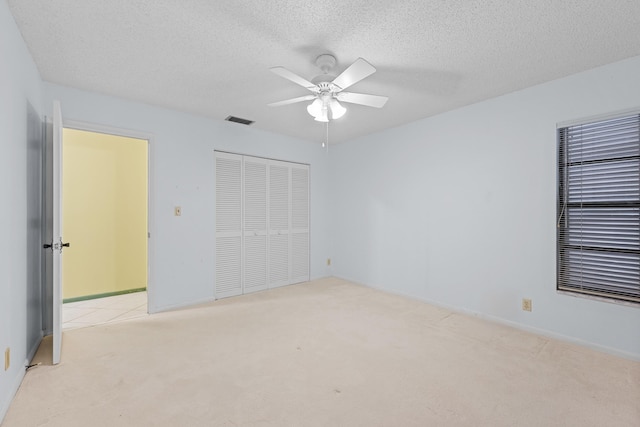 unfurnished bedroom featuring ceiling fan, a closet, light colored carpet, and a textured ceiling