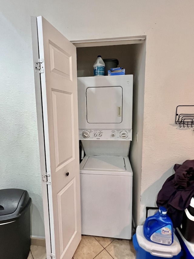 clothes washing area featuring light tile patterned floors, stacked washing maching and dryer, and laundry area