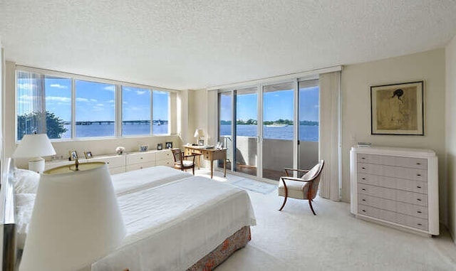 bedroom featuring light carpet, access to outside, a textured ceiling, and a water view