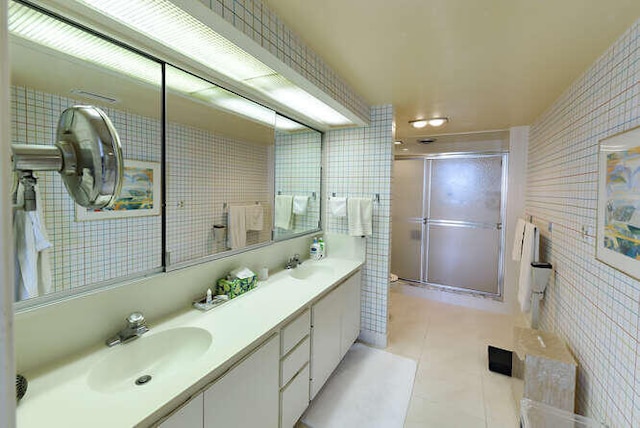 bathroom with tile patterned flooring, vanity, a shower with shower door, and tile walls