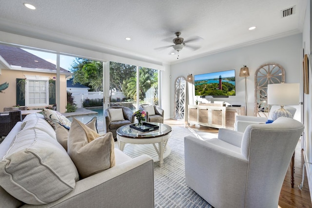 living room featuring light wood-type flooring, ornamental molding, a textured ceiling, and ceiling fan