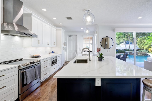 kitchen with sink, a large island with sink, hanging light fixtures, wall chimney range hood, and appliances with stainless steel finishes