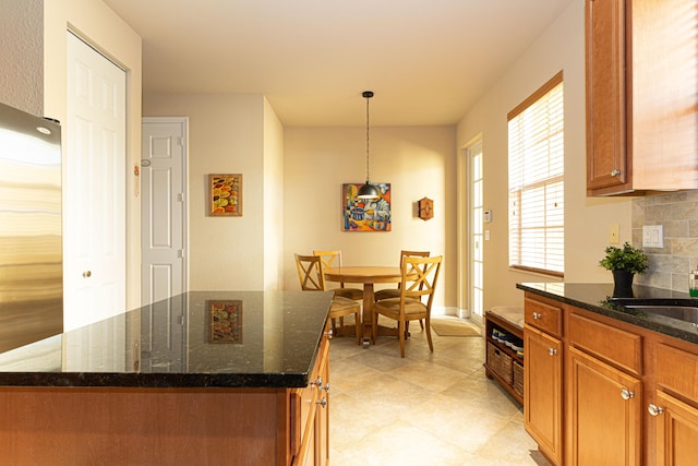 kitchen with stainless steel refrigerator, a center island, dark stone countertops, pendant lighting, and decorative backsplash