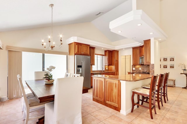 kitchen with light stone countertops, kitchen peninsula, a chandelier, pendant lighting, and appliances with stainless steel finishes