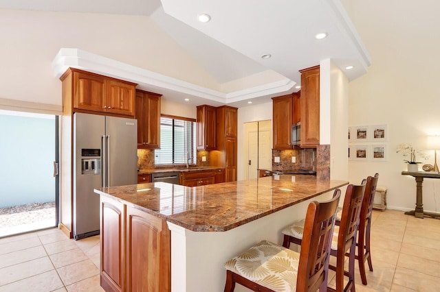 kitchen featuring stainless steel appliances, kitchen peninsula, dark stone counters, a breakfast bar, and light tile patterned floors