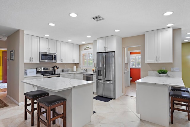 kitchen with a kitchen bar, a wealth of natural light, white cabinetry, and stainless steel appliances