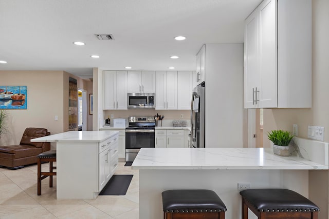 kitchen with white cabinetry, light stone counters, kitchen peninsula, a breakfast bar area, and appliances with stainless steel finishes