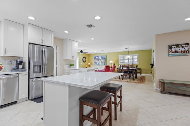 kitchen featuring white cabinets, hanging light fixtures, a breakfast bar area, light stone countertops, and stainless steel appliances