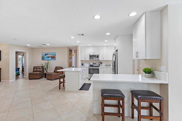 kitchen with white cabinetry, stainless steel appliances, kitchen peninsula, a breakfast bar, and light tile patterned flooring