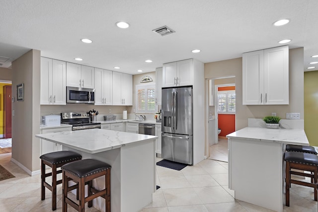 kitchen featuring white cabinets, a kitchen bar, stainless steel appliances, and light stone countertops