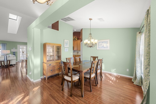 dining room with dark hardwood / wood-style flooring, a notable chandelier, and vaulted ceiling with skylight