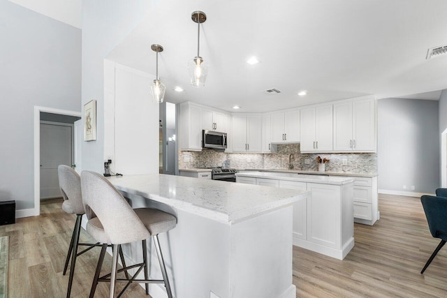 kitchen featuring white cabinetry, tasteful backsplash, appliances with stainless steel finishes, kitchen peninsula, and pendant lighting