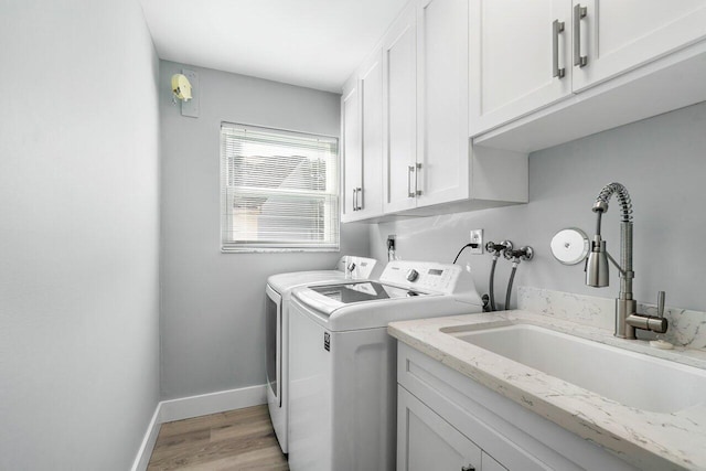 clothes washing area with washer and clothes dryer, cabinets, sink, and light hardwood / wood-style floors