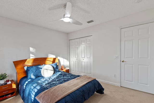 bedroom with ceiling fan, light colored carpet, a textured ceiling, and a closet