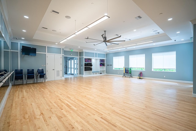 exercise area featuring ceiling fan, light wood-type flooring, ornamental molding, and a tray ceiling