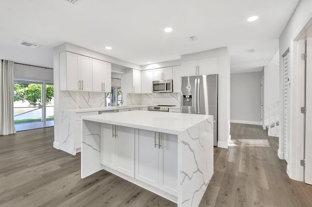 kitchen with stainless steel appliances, white cabinets, a center island, and light stone countertops