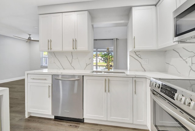 kitchen with stainless steel appliances, sink, white cabinets, ceiling fan, and light stone countertops