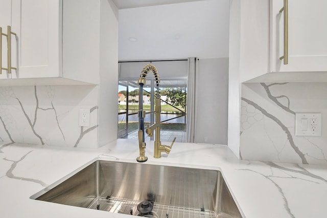 details featuring sink, white cabinets, tasteful backsplash, and light stone countertops