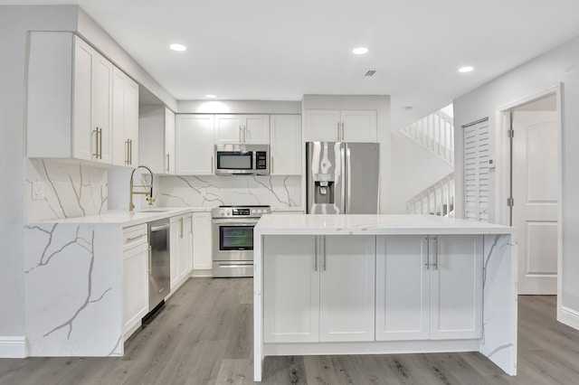 kitchen with sink, a center island, white cabinetry, light stone countertops, and appliances with stainless steel finishes