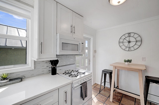 kitchen with backsplash, ornamental molding, white appliances, white cabinetry, and wood walls